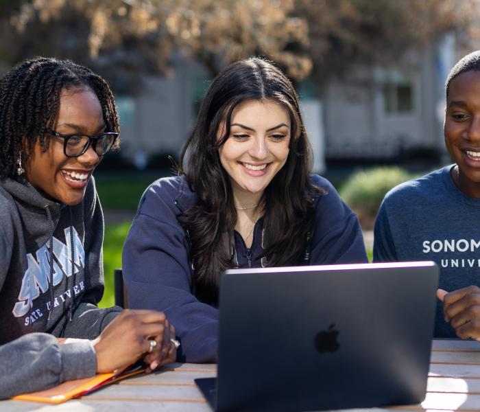 Three students studying at a table and looking at a computer