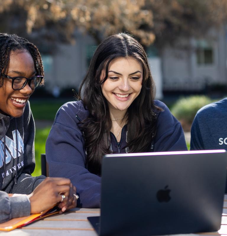 Three students studying at a table and looking at a computer